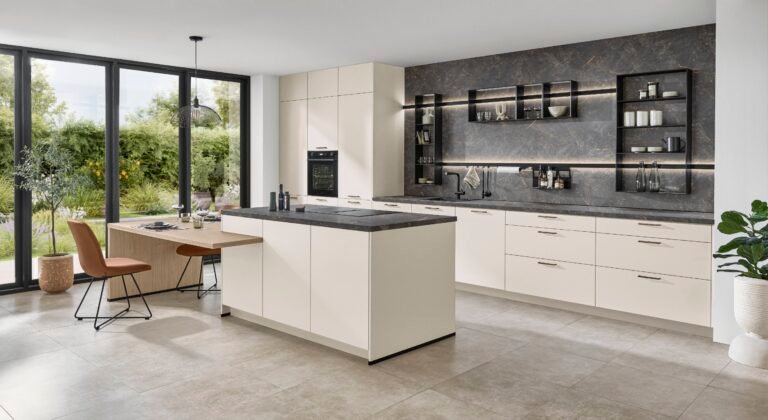 Cocina moderna en Alicante con isla central, pared efecto piedra oscura, muebles en color crema y comedor integrado con vistas al jardín.