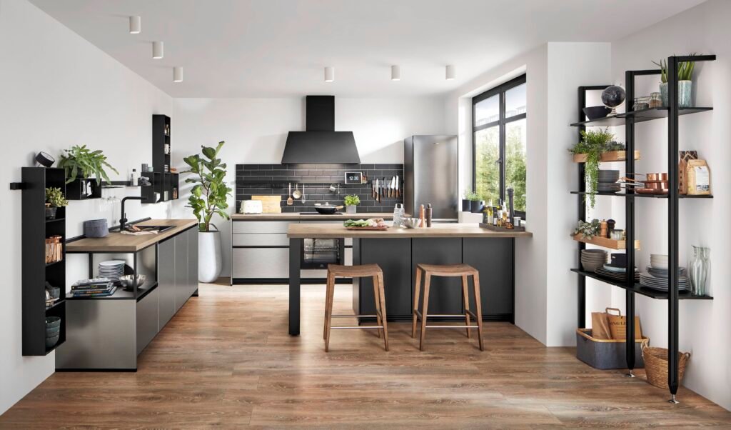 Cocina moderna estilo industrial en Alicante con muebles en acero inoxidable, isla central con taburetes de madera, baldas negras y suelo de madera cálida.