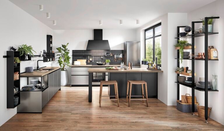 Cocina moderna estilo industrial en Alicante con muebles en acero inoxidable, isla central con taburetes de madera, baldas negras y suelo de madera cálida.