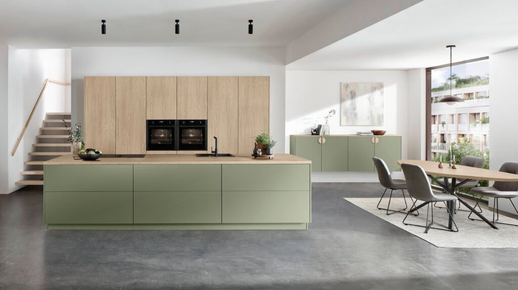 Cocina moderna en Alicante con isla central en color verde salvia, muebles de madera clara, comedor integrado y diseño minimalista luminoso